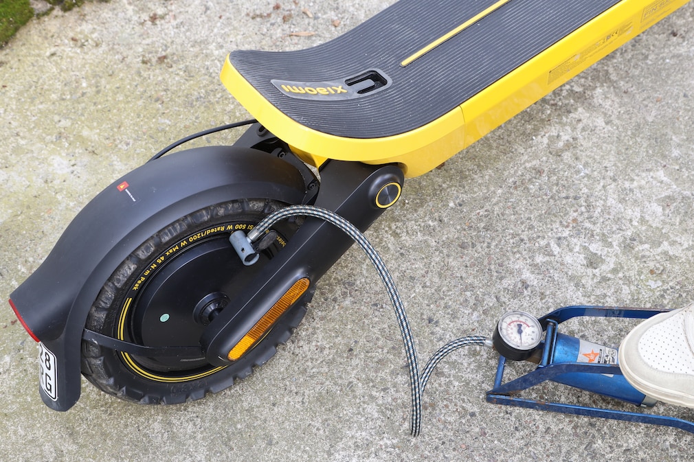 Detailaufnahme eines Hinterrades eines E-Scooters mit Ausschnitt eines Fußes der eine Fußpumpe betätigt.