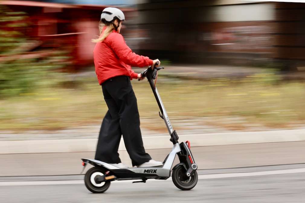 Person fährt mit E-Scooter durch einen Kreisverkehr, der Hintergrund ist verschwommen.