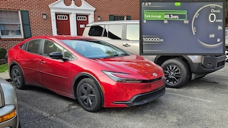 Toyota Prius LE in rot geparkt vor einem Backsteinhaus und der Tacho, der 100.000 Meilen Laudleistung anzeigt.