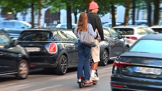 Halterhaftung für E-Scooter ratifiziert. Ein junges Paar faehrt gemeinsam auf einem E-Scooter durch eine staedtische Strasse in Muenchen