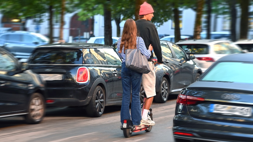 Halterhaftung für E-Scooter ratifiziert. Ein junges Paar faehrt gemeinsam auf einem E-Scooter durch eine staedtische Strasse in Muenchen