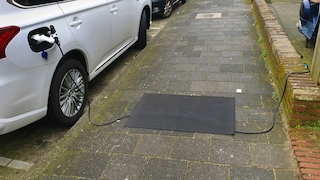 Ladekabel zum Aufladen eines E-Autos liegt auf dem Gehweg, Fussmatte verhindert stolpern, charging cable for an e-car lying on the sidewalk, a mat preventing to stumble