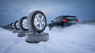 Auto fährt an Reifenstapel im Schnee vorbei.