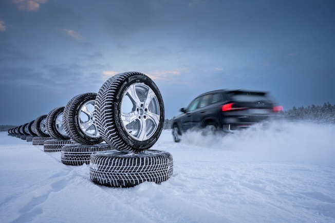 Auto fährt an Reifenstapel im Schnee vorbei.
