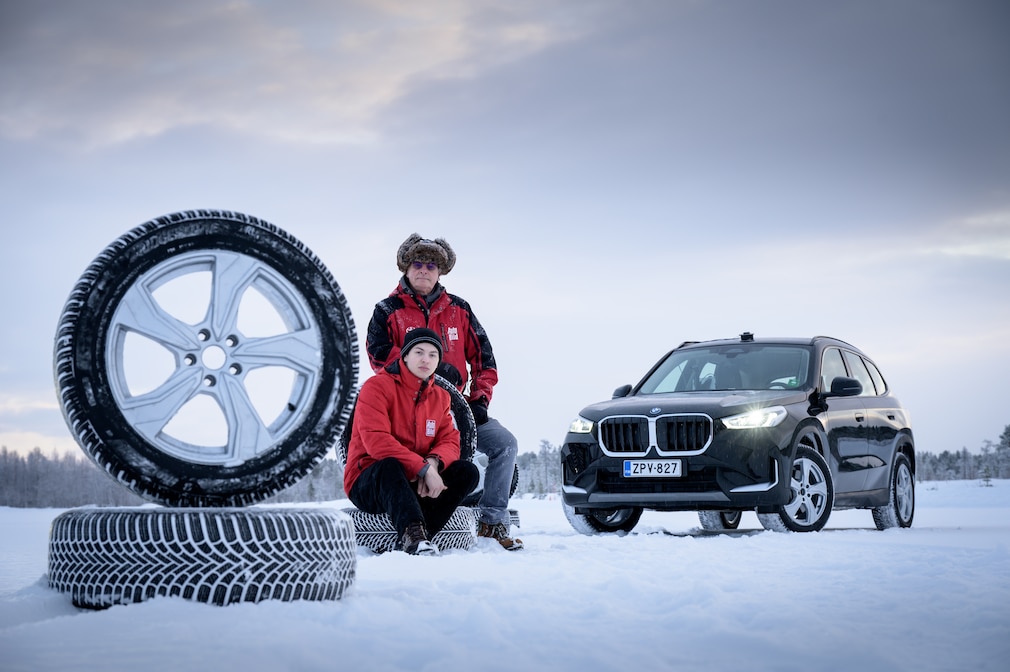 Redakteure sitzen auf einem Reifenstapel, im Hintergrund ein BMW X1