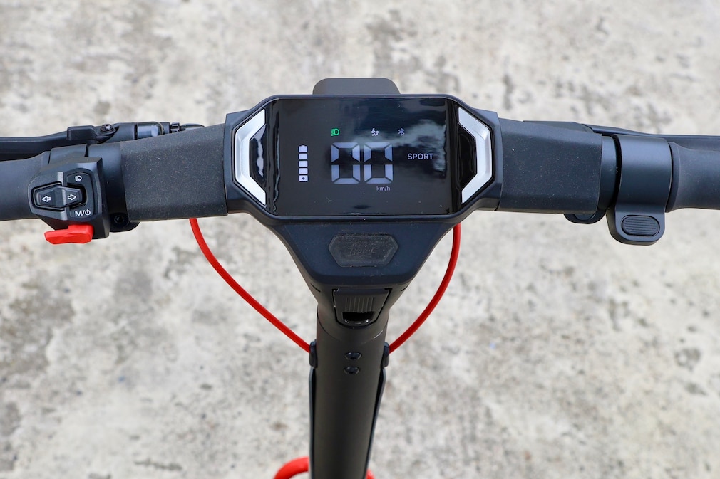 Blick aus Fahrersicht auf Cockpit und Lenker eines E-Scooters. Das Display zeigt Geschwindigkeit, Akkustand und Fahrinformationen an. Bedienelemente für Licht, Blinker und Fahrmodi sitzen direkt am Lenker.