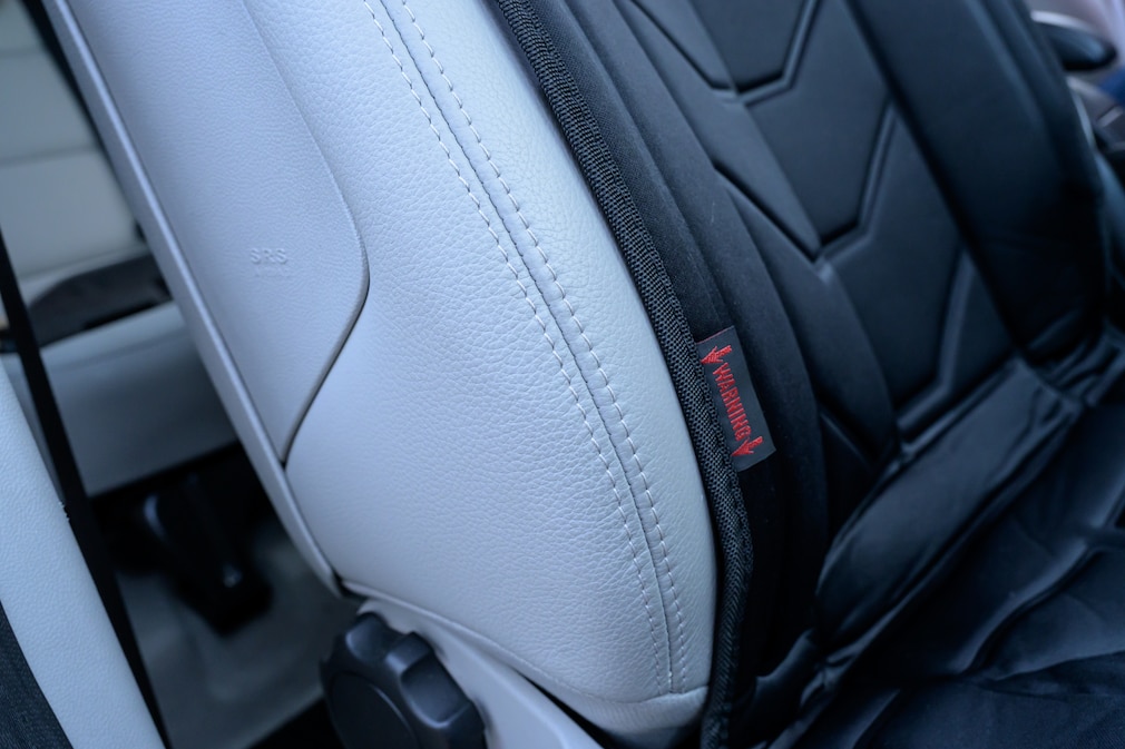 Detailaufnahme der Seitenwange eines Autositzes mit Heizmatte an der ein Schild auf den Airbag hinweist
