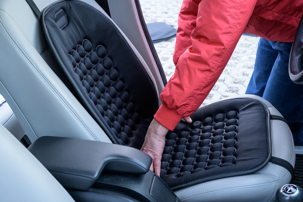 Eine Person montiert eine Sitzheizmatte auf einem Fahrzeugsitz und richtet sie an der Sitzfläche aus