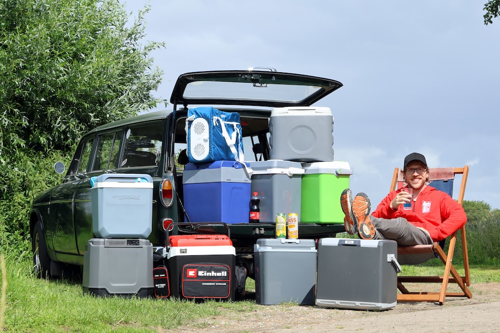 Redakteur sitzt auf Liegestuhl, neben ihm Kühlboxen und ein Oldtimer.