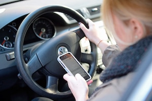 Eine Frau sitzt am 02.10.2015 in Düsseldorf (Nordrhein-Westfalen) im Auto am Steuer und liest Nachrichten auf ihrem Smartphone. Bei einem Pressetermin informierte der nordrhein-westfälische Innenminister über die Gefahren von Handy- und Smartphonenutzung am Steuer.