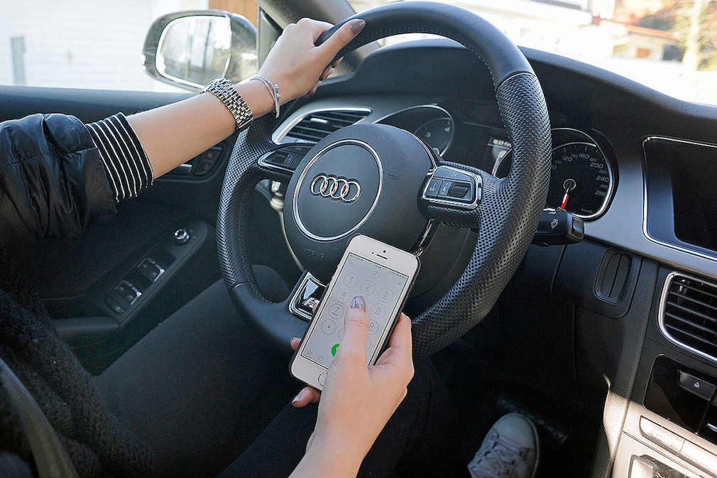 Benutzung eines Mobiltelefons am Steuer eines PKW. Eine Hand am Lenkrad, die andere hält ein Handy, Smartphone, Mobiltelefon.