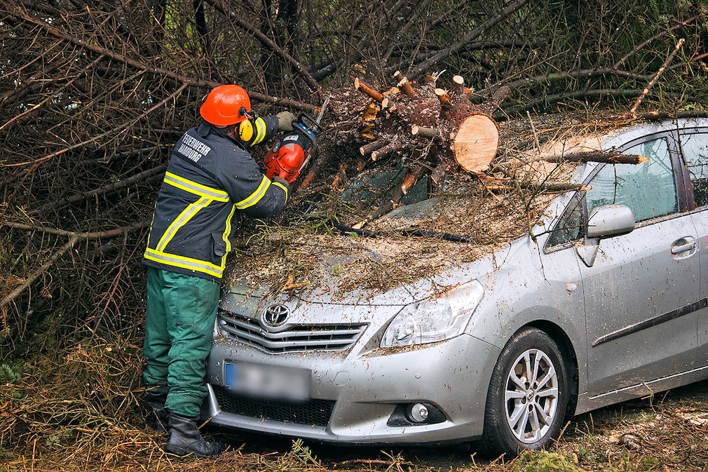 Ein Feuerwehrmann zersägt am 05.05.2015 in Hamburg-Rahlstedt einen auf ein Auto gestürzten Baum