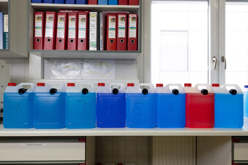 Laborsituation: 8 neutrale Kanister, aufgereiht und gefüllt mit verschiedenfarbigen Flüssigkeiten.