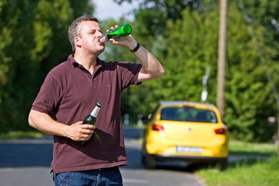 Mann trinkt Bier vor einem Auto